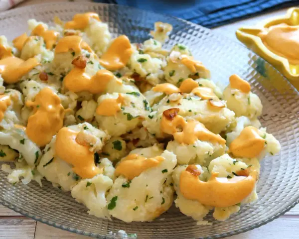 Coliflor al ajillo con salsa cremosa, adornada con perejil fresco y trocitos de ajo crujiente.