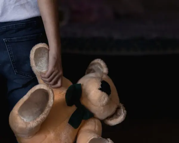Main d'enfant tenant un ours en peluche. Un signalement enfance en danger en ligne peut aider.