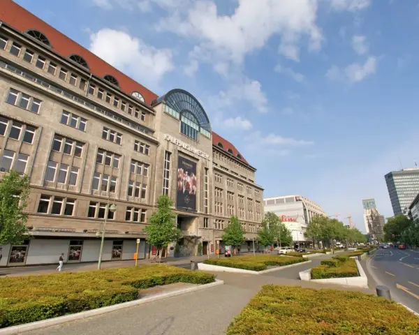 Das KaDeWe Berlin, ein imposantes Gebäude mit vielen Fenstern, steht unter einem blauen Himmel mit Wolken.