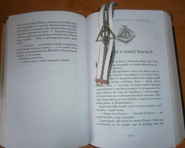 Otwarta książka z zakładką w kształcie symbolu Insygniów Śmierci. Tekst opowiada baśń o trzech braciach.