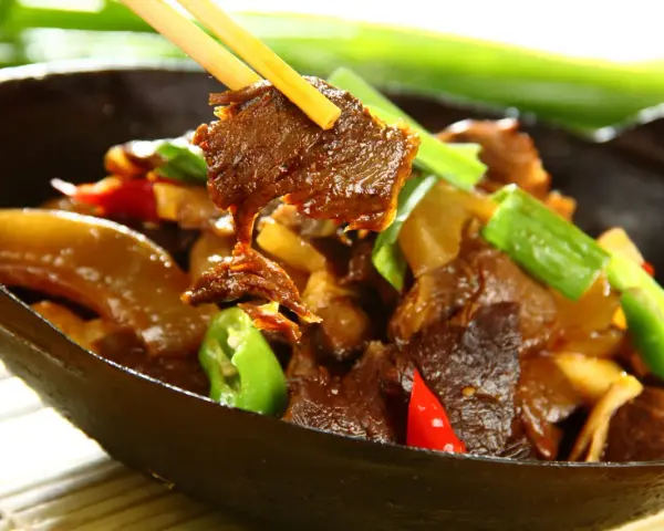 Chopsticks podnoszą kawałek aromatycznej wołowiny po chińsku z miski pełnej pysznego dania z warzywami.