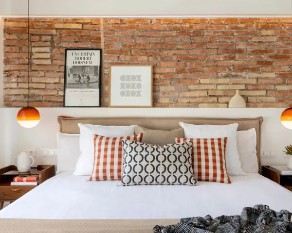 Ideas para decorar la pared de la cabecera de la cama: ladrillo visto, cuadros y lámparas naranjas.