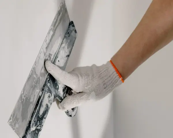 Mano enguantada alisando masilla para tapar agujeros en la pared.