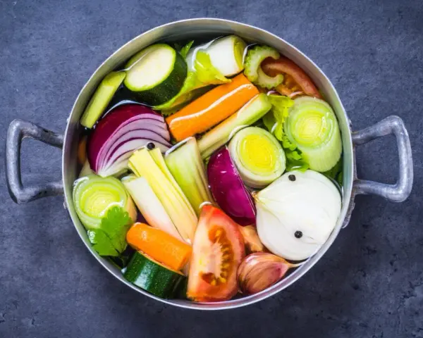 Olla con verduras cortadas en trozos: cebolla, zanahoria, calabacín, puerro, tomate y ajo.