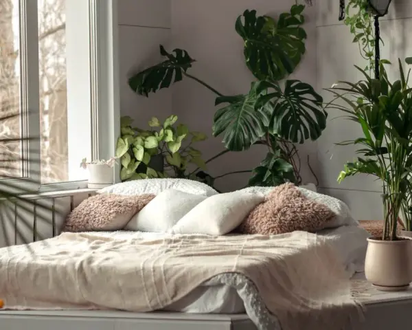 Sypialnia z bujną roślinnością, gdzie różnica między stylem tropikalnym a "urban jungle" w aranżacji wnętrz jest subtelna. Duże liście monstery i palmy tworzą zieloną oazę.