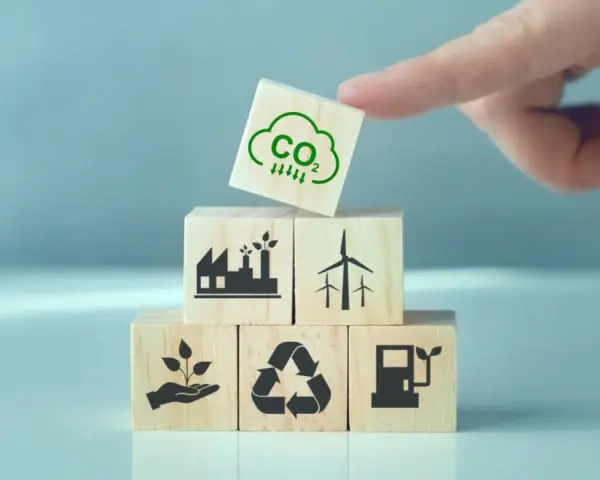 Klocki symbolizujące zielony ład: fabryka, wiatraki, sadzonka, recykling, paliwo. Na górze kostka z chmurką CO2 i strzałkami w dół.