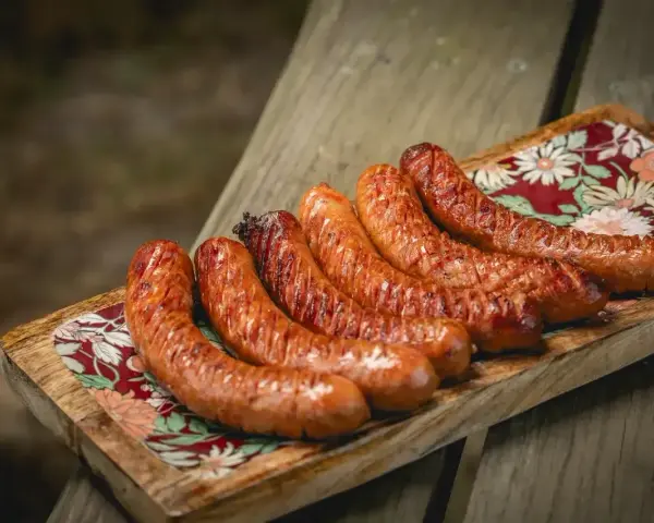 Apetyczna kiełbasa z grilla, rumiana i soczysta, ułożona na drewnianej desce z kolorowym wzorem.