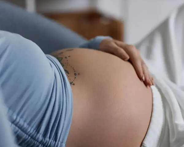 Dłoń delikatnie głaszcze ciążowy, twardy brzuch z tatuażem.