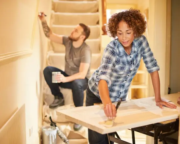 Pareja renovando su hogar con una reforma sin obras. Ella pinta una puerta, él la pared.