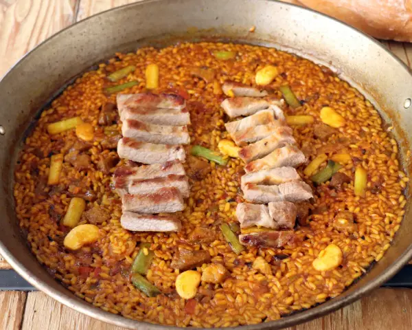 Arroz con secreto, un plato de paella con cerdo tierno y verduras crujientes, listo para ser disfrutado.