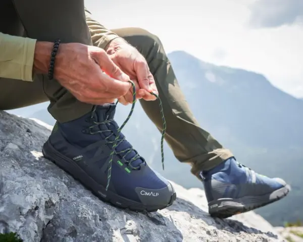 Uomo lega i lacci di scarponi da hiking su roccia, pronto per il trekking in montagna.