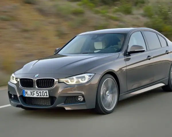 Szary sedan BMW F30 z dynamicznymi silnikami pędzi po drodze, ukazując sportowy charakter.