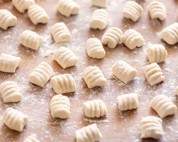 Gnocchi di ricotta freschi, pronti per essere cucinati, spolverati di farina su un tagliere di legno.