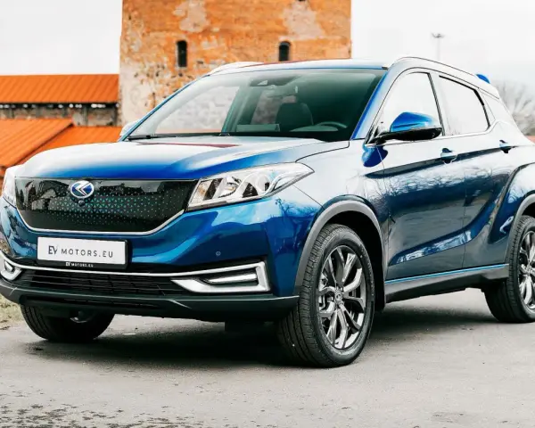 Błękitny SUV EV Motors.eu z charakterystycznym grillem, zaparkowany przed zabytkowym budynkiem z cegły.