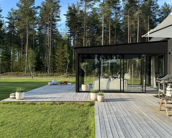 Modernt uterum med glaspartier och träaltan, perfekt för att bygga ett drömhem vid skogen.