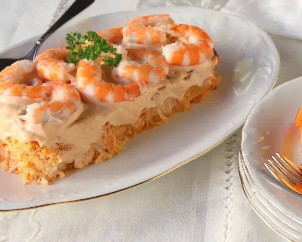 Delicioso pudin de pescado cubierto con crema y camarones, decorado con perejil.