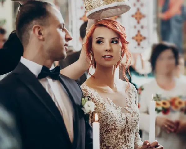 Para ślubna w kościele, z koroną nad głowami. Panna młoda w koronkowej sukni, pan młody w garniturze. W tle goście. Zastanawiasz się, jakie dokumenty do ślubu?