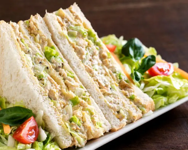 Sándwich de pollo cortado en triángulos, relleno de pollo desmenuzado y lechuga, acompañado de ensalada fresca.