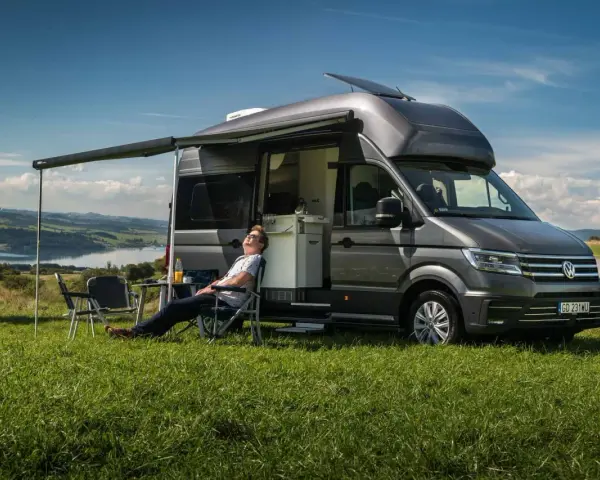 Mężczyzna odpoczywa przy kamperze VW California. Wymiary tego pojazdu pozwalają na komfortowe podróżowanie i biwakowanie.