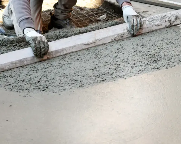 Ręce w rękawiczkach wyrównują świeży beton na taras za pomocą łaty.