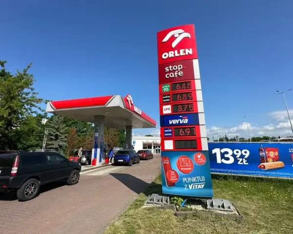 Stacja paliw Orlen z cennikiem paliw: benzyna 95 za 6.48 zł, diesel za 6.89 zł, LPG za 3.75 zł. Obok reklama hot doga i napoju.
