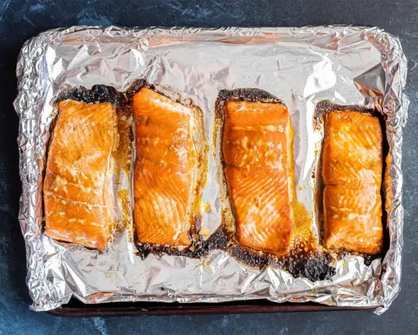 Cztery kawałki łososia pieczone na folii aluminiowej, gotowe do przygotowania sushi.