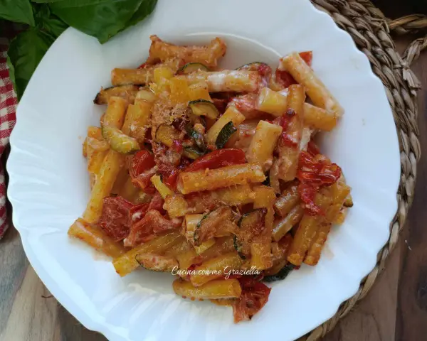 Piatto di pasta con zucchine e pomodorini, condita con formaggio grattugiato e basilico fresco.