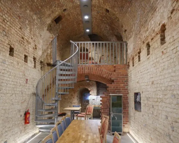 Wnętrze restauracji Srebrna Góra z kamiennymi ścianami, kręconymi schodami i drewnianymi stołami.
