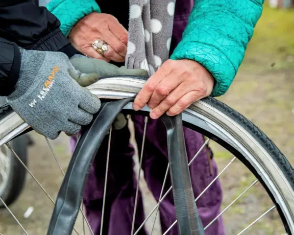 Två personer byter cykelslang. En med grå handske och en med grön jacka och prickig scarf.