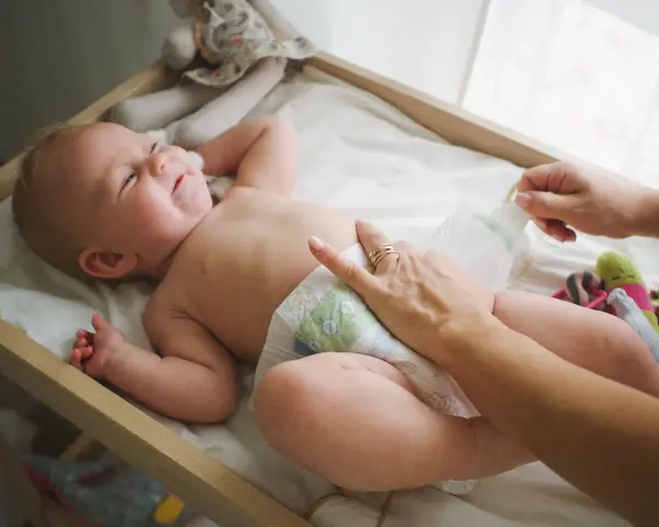 Radość noworodka podczas pielęgnacji. Mama zmienia pieluszkę, maluch uśmiecha się, leżąc na przewijaku wśród zabawek.