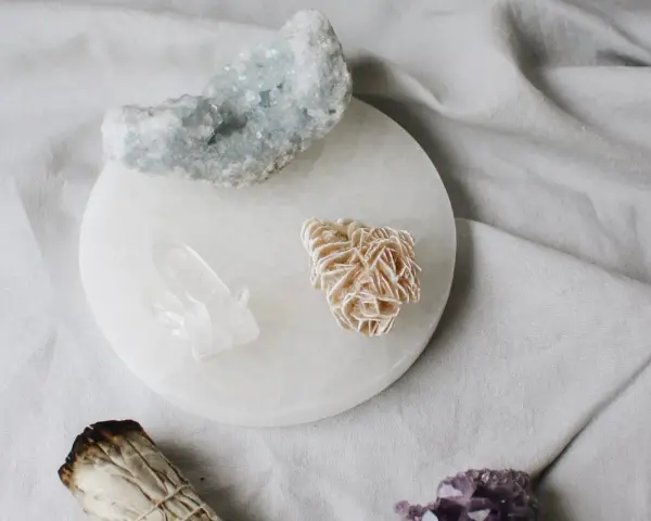 Cristales de selenita, cuarzo y amatista sobre un plato de selenita, junto a un manojo de salvia. Guía para saber como limpiar la selenita.