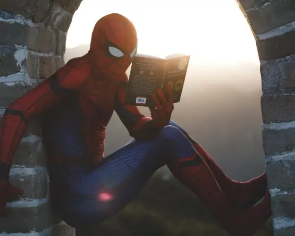 Spider-Man w czerwonym stroju siedzi na murze i czyta książkę. Czy komiks to utwór literacki? Nawet superbohaterowie potrzebują chwili wytchnienia i wiedzy.