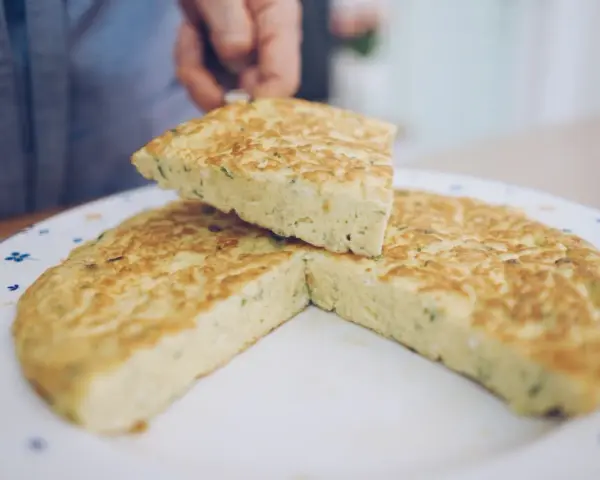 Una fetta di frittata, preparata con la ricetta perfetta, viene sollevata da un piatto decorato.