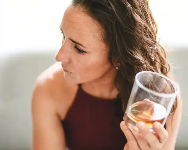 Kobieta zamyślona trzyma szklankę z bursztynowym płynem. Zastanawia się, jak ograniczyć alkohol.