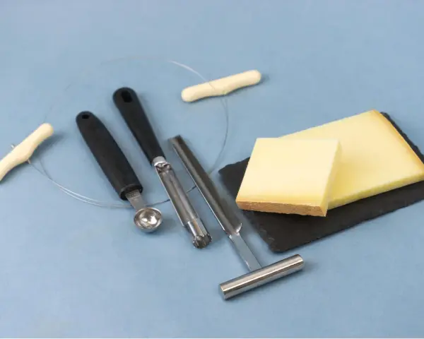Des morceaux de fromage, des outils pour le découper et une ficelle. L'origine du fromage la dent du chat est un mystère savoureux.