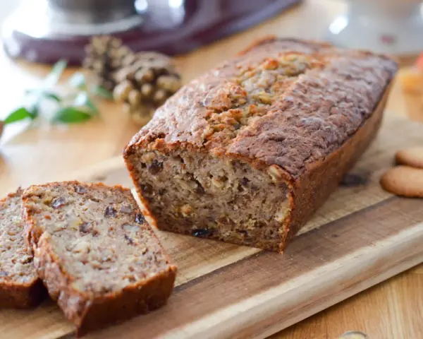 Un délicieux cake banane, coupé en tranches, sur une planche en bois. Des noix et des biscuits complètent cette gourmandise.