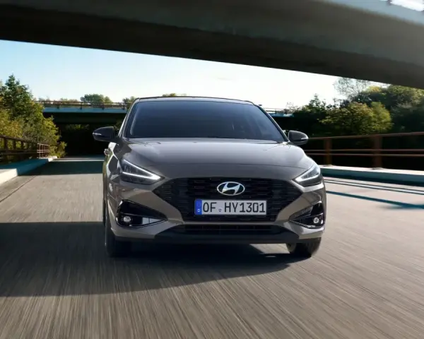 Szary Hyundai i30 1.4 benzyna pędzi po drodze pod mostem, otoczony zielenią.