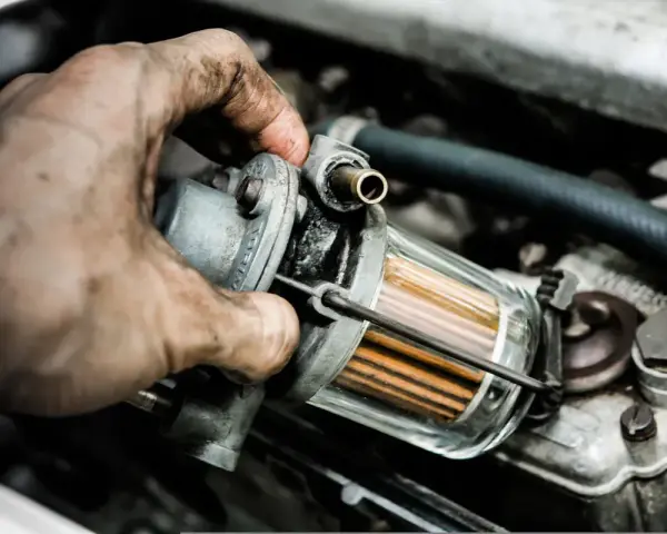 Brudna ręka mechanika wymienia filtr paliwa, by wyeliminować nierówną pracę silnika na wolnych obrotach LPG.