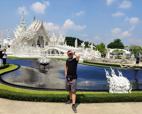 Mężczyzna pozuje przed olśniewającą białą świątynią Wat Rong Khun w Chiang Rai.