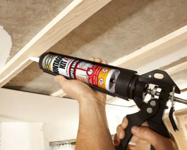 Uso di una pistola per colla per fissare il cartongesso a una struttura in legno.