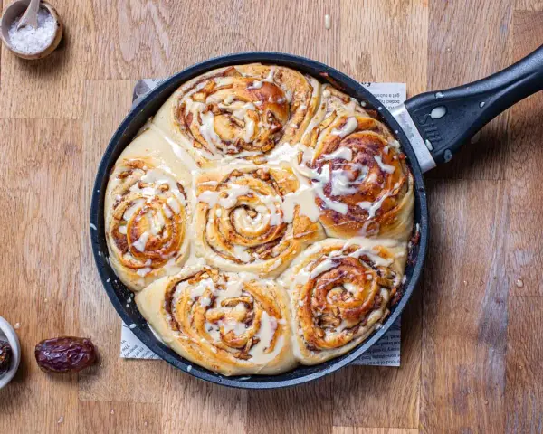 Frisch gebackene Zimtschnecken mit Apfelstückchen und Zuckerguss in einer Pfanne. Ein köstliches Apfel Zimtschnecken Rezept zum Nachbacken.