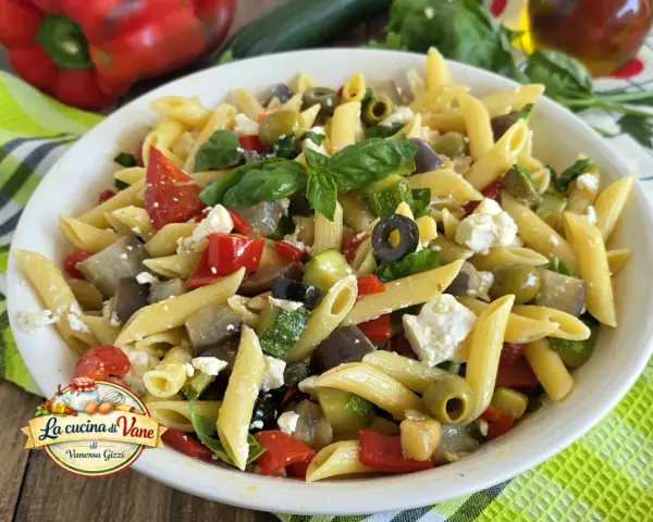 Pasta fredda con feta, peperoni, zucchine, melanzane e olive nere. Un piatto estivo colorato e saporito.