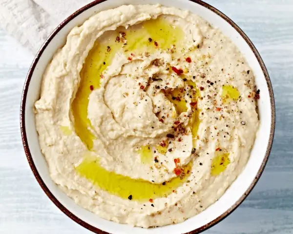 Kremowy, gładki hummus polany oliwą i posypany przyprawami. Idealny do maczania pieczywa.