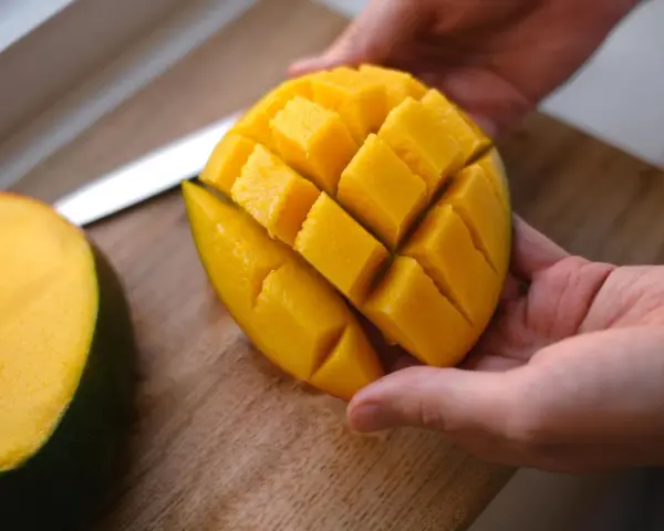 Hände halten ein perfekt geschnittenes Mango-Viertel, bereit zum Genießen. Das Fruchtfleisch ist in Würfel geschnitten, was das Mango schneiden erleichtert.