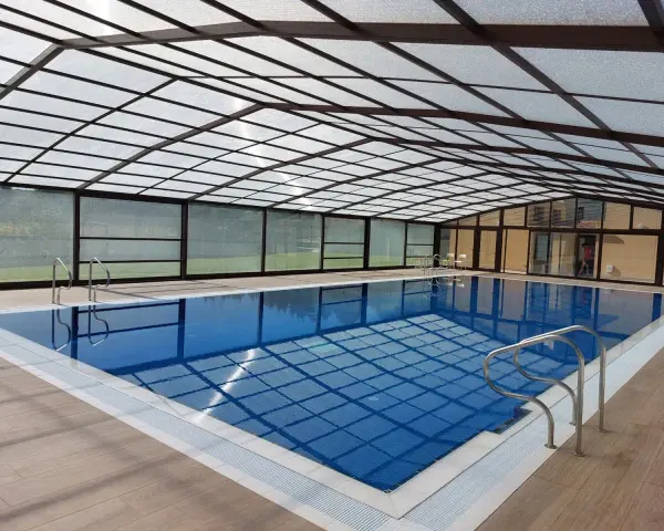 Una piscina cubierta con techo transparente y paredes de cristal, ideal para disfrutar todo el año. Estos porches para piscinas ofrecen un espacio acogedor.
