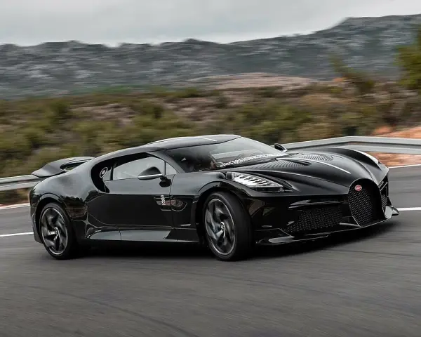 Czarny Bugatti La Voiture Noire pędzi po krętej drodze, otoczony przez górzysty krajobraz.