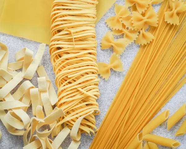 Różne rodzaje suchego makaronu: tagliatelle, farfalle, spaghetti, penne i płaty lasagne. Zastanawiasz się, ile waży makaron po ugotowaniu vs suchy?