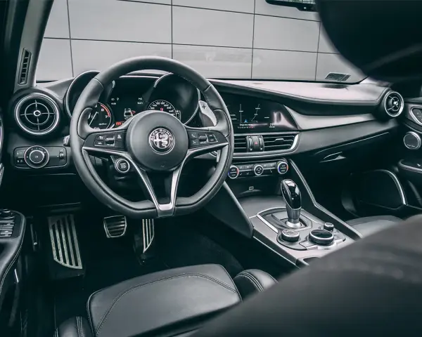 Wnętrze luksusowego samochodu Alfa Romeo. Kierownica, deska rozdzielcza i dźwignia zmiany biegów. Ta fotografia samochodowa oddaje styl i komfort.