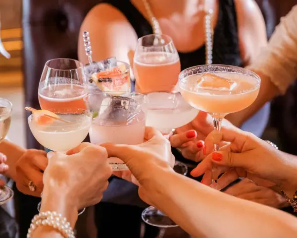 Frauen stoßen mit bunten Cocktails an. Ein fröhlicher Anlass für Day Drinking mit Freundinnen.