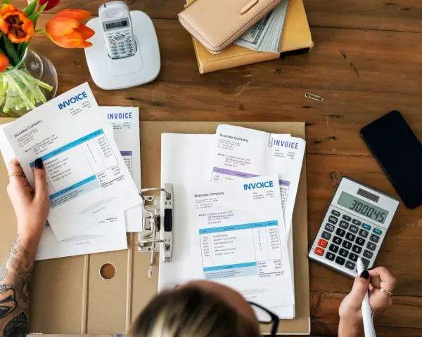 Manos revisando facturas y calculando el total. Aprende como hacer una factura a mano.